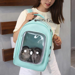 Person holding a light blue pet carrier with a cat inside, wearing a white shirt with text.