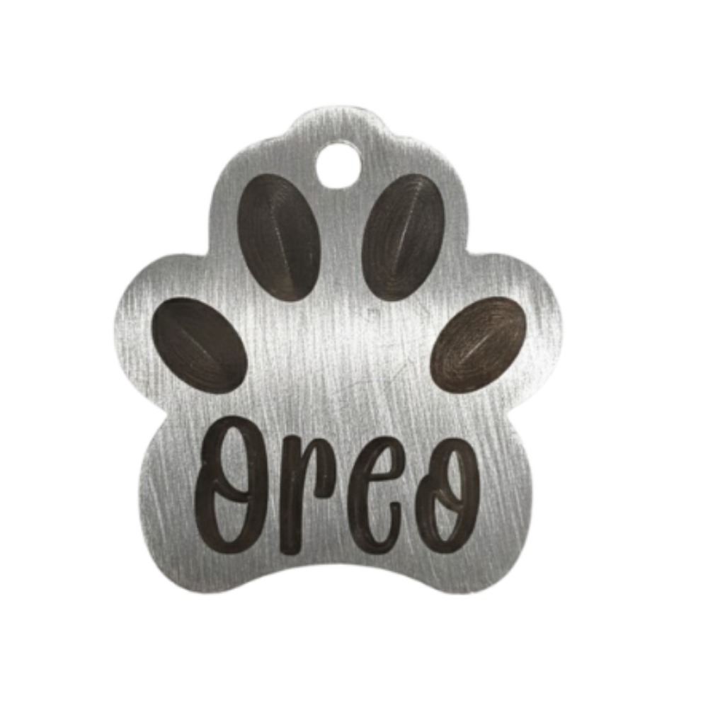 Metal paw-shaped pet tag with 'Oreo' engraved on a white background