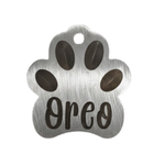Metal paw-shaped pet tag with 'Oreo' engraved on a white background