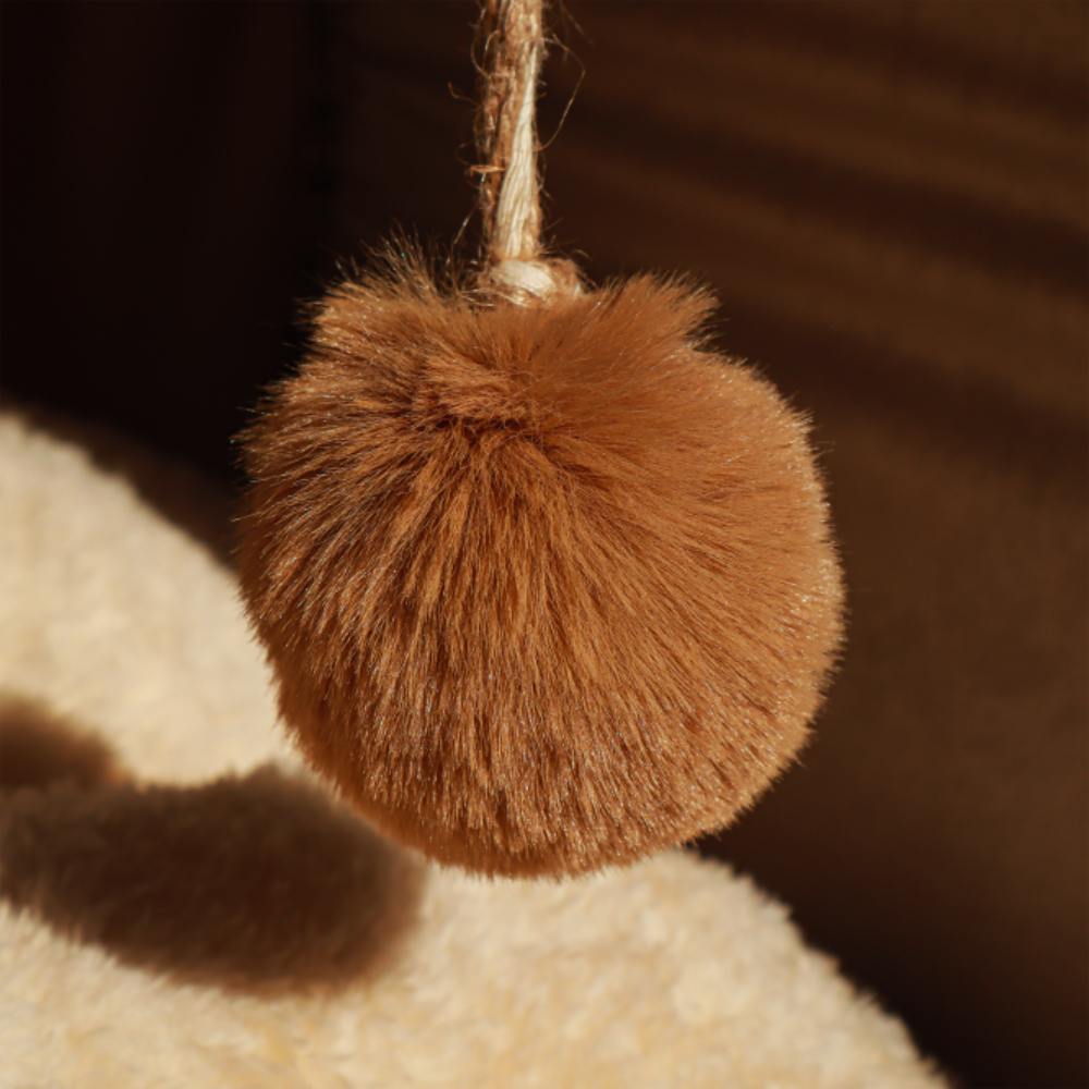 Brown fuzzy pom-pom hanging on a textured surface