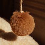 Brown fuzzy pom-pom hanging on a textured surface