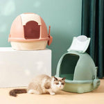 Two cat litter boxes, one pink and one green, with a cat sitting between them on a light-colored floor.