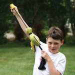 Child holding a toy bow and arrow outdoors with greenery in the background