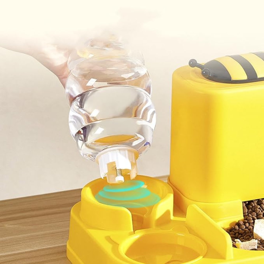Yellow bee-shaped pet feeder with clear water dish on a wooden surface.