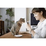 Woman holding a smartphone with a cat looking at it in a home setting