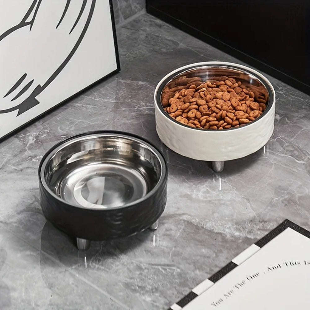 Two pet bowls on a marble surface, one black and one white with a silver interior, containing dry cat food.
