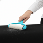 Hand using a blue pet hair removal roller on a black surface with visible pet hair.
