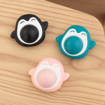 Three cartoon-style penguin phone holders on a wooden surface