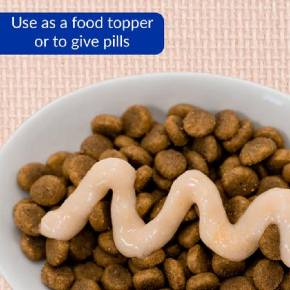 Dog food with a white sauce on top in a bowl, with text indicating use as a food topper or for giving pills.
