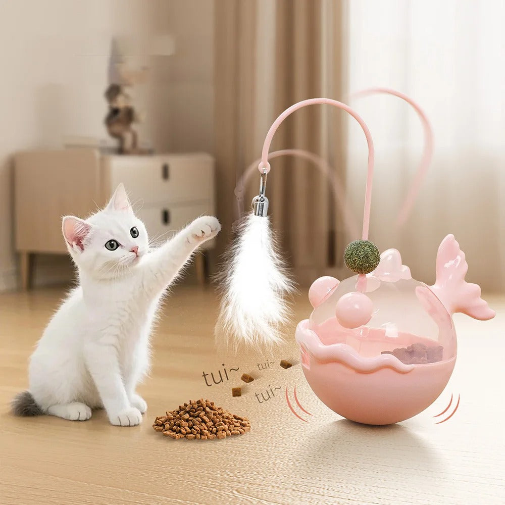 White kitten playing with a pink cat toy on a wooden floor.