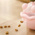 Dog food scattered on a wooden surface next to a pink pet bowl.