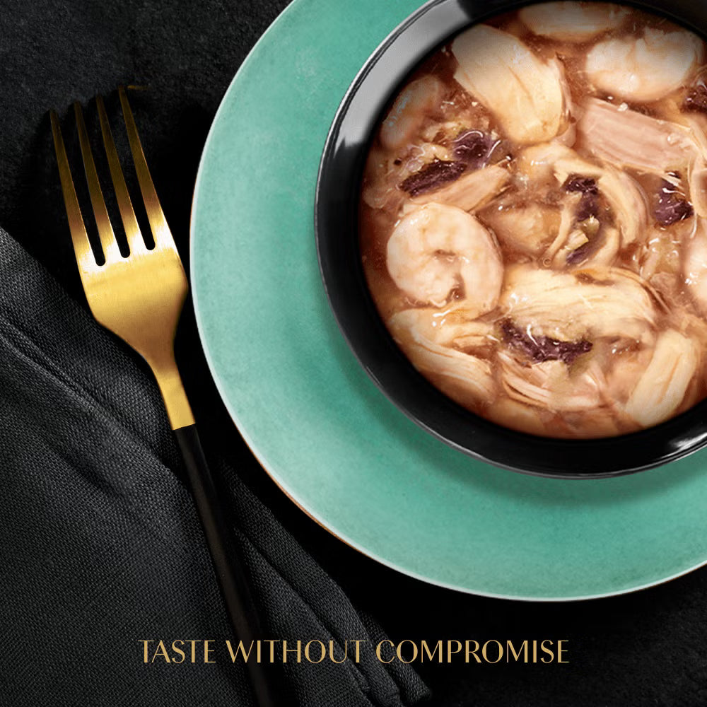 Bowl of soup with shrimp on a green plate with a gold fork, on a black background.