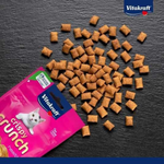Vitakraft Crispy Crunch cat food on a black surface with packaging.