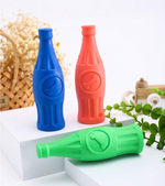 Three colorful bottle-shaped dog toys on a white surface with a natural background.