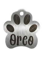 Metal paw-shaped pet tag with 'Oreo' engraved on a white background