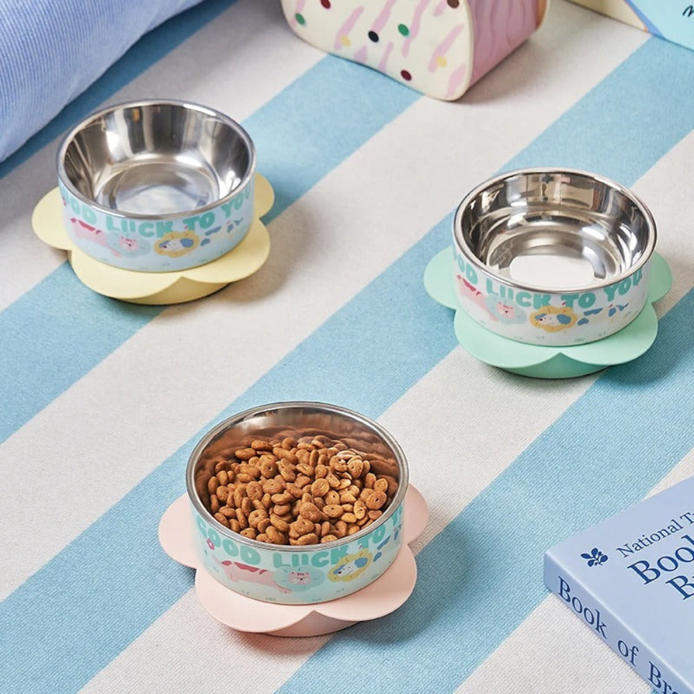 Three stainless steel bowls with colorful bases on a striped surface, one filled with pet food.