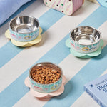 Three stainless steel bowls with colorful bases on a striped surface, one filled with pet food.