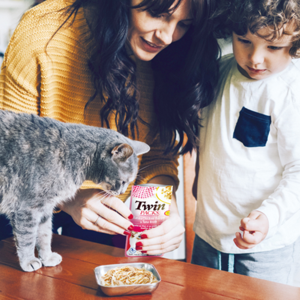Woman and child with a cat and Twin Pack pet food at a table